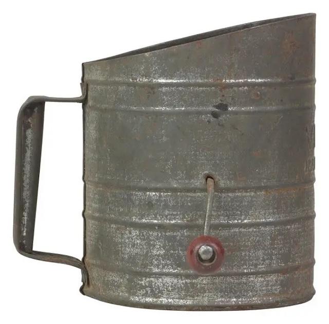 A well-used old-fashioned flour sifter, with a worn handle and weathered exterior, showing its age and long history in kitchens